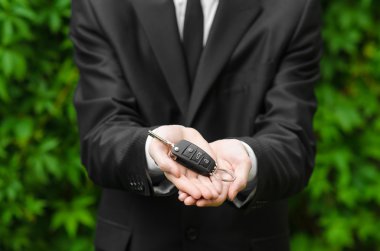 Yeni araba ve iş Tema: siyah elbiseli bir adam yeni bir araba anahtarları yeşil çim bir arka plan üzerinde tutar.