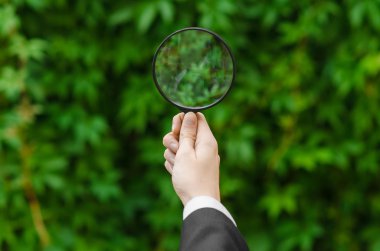 Search and business topic: hand in a black suit holding a magnifying glass on a background of green grass