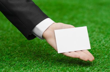 Discounts and business topic: hand in a black suit holding a white blank card on green grass background