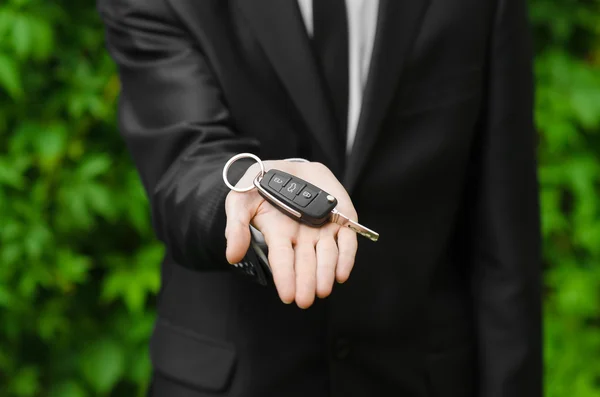 Новая машина и деловая тема: человек в черном костюме держит ключи от новой машины на фоне зеленой травы — стоковое фото