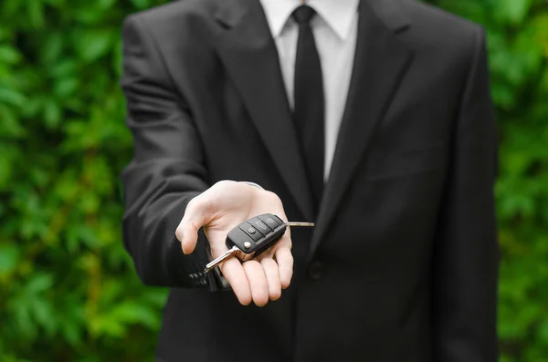 Nieuwe auto en zakelijke thema: een man in een zwart pak omvat de sleutels van een nieuwe auto tegen een achtergrond van groen gras — Stockfoto