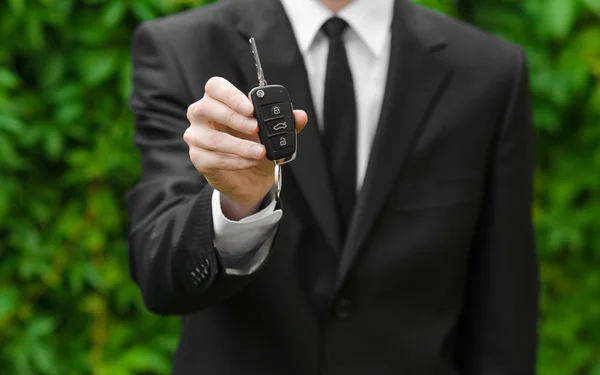 Nieuwe auto en zakelijke thema: een man in een zwart pak omvat de sleutels van een nieuwe auto tegen een achtergrond van groen gras — Stockfoto