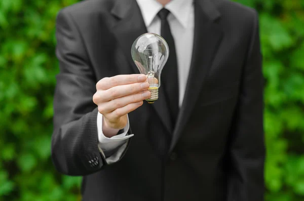 Eletricidade e tema de negócios: um homem de terno preto segurando uma lâmpada contra um fundo de grama verde — Fotografia de Stock