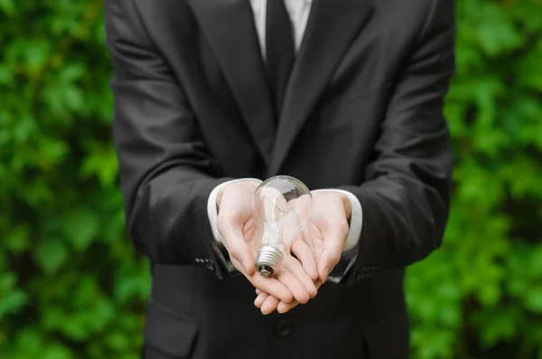 Electricity and business theme: a man in a black suit holding a light bulb against a background of green grass — Zdjęcie stockowe