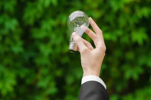 Eletricidade e tema de negócios: um homem de terno preto segurando uma lâmpada contra um fundo de grama verde — Fotografia de Stock