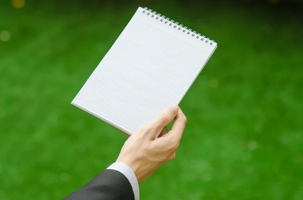 Giorno di conoscenza e argomento di affari: la mano dell'uomo in un abito nero che tiene un notebook e una matita vista dall'alto su uno sfondo di erba verde — Foto Stock