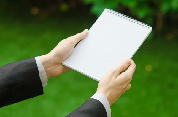 Giorno di conoscenza e argomento di affari: la mano dell'uomo in un abito nero che tiene un notebook e una matita vista dall'alto su uno sfondo di erba verde — Foto Stock