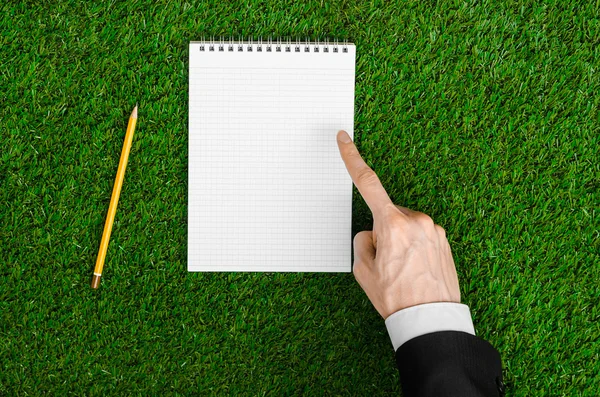 Giorno di conoscenza e argomento di affari: la mano dell'uomo in un abito nero che tiene un notebook e una matita vista dall'alto su uno sfondo di erba verde — Foto Stock