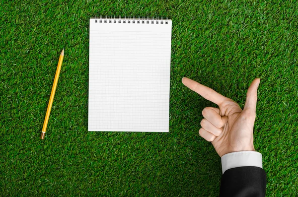 Day of knowledge and business topic: the hand of man in a black suit holding a notebook and pencil top view on a background of green grass — 스톡 사진