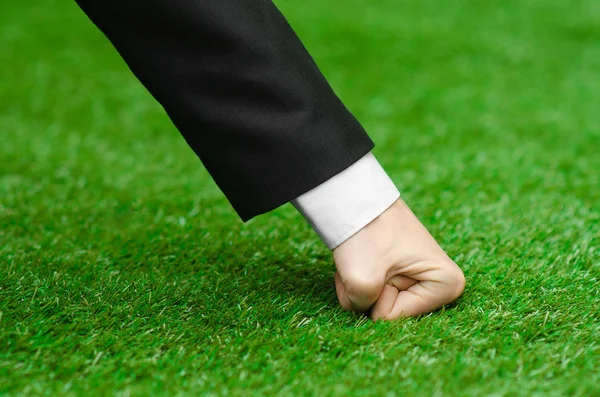 Nature and business topic: the hand of man in a black suit presses his fist green grass