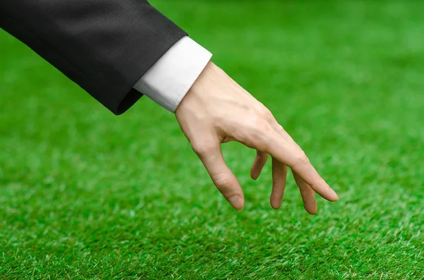 Charakter i temat: ręka mężczyzny w czarnym garniturze wskazuje zielona trawa — Zdjęcie stockowe