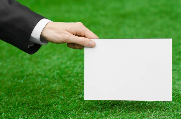 Discounts and business topic: hand in a black suit holding a white blank card on green grass background — Stock fotografie