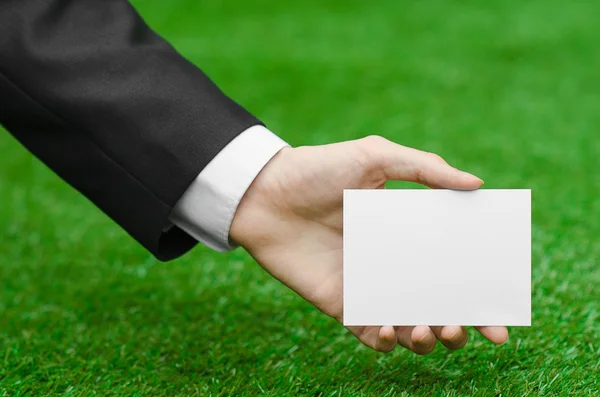 Discounts and business topic: hand in a black suit holding a white blank card on green grass background — Stock fotografie