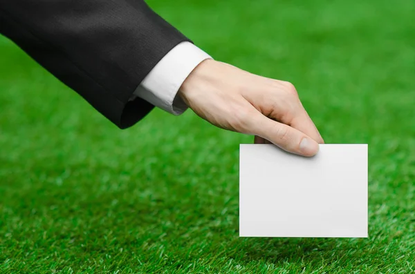 Discounts and business topic: hand in a black suit holding a white blank card on green grass background — 스톡 사진