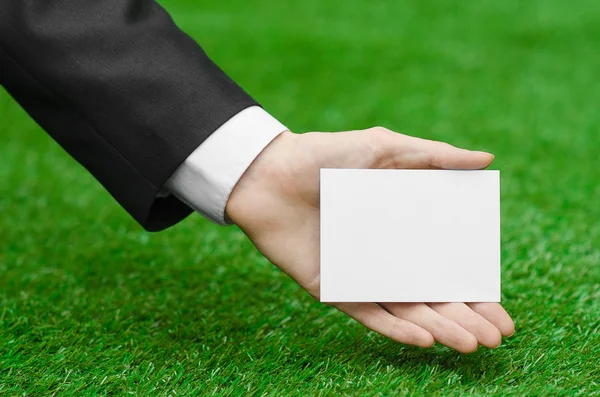 Discounts and business topic: hand in a black suit holding a white blank card on green grass background — Stock fotografie