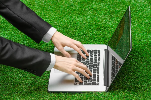 Work outdoors and businessman topic: human hands show the gestures in a black suit and an open notebook on a background of green grass