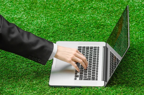 Work outdoors and businessman topic: human hands show the gestures in a black suit and an open notebook on a background of green grass