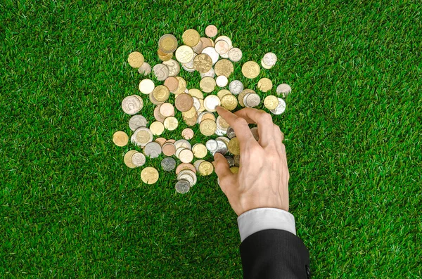 Money and Finance Topic: Money coins and human hand in black suit showing gesture on a background of green grass top view