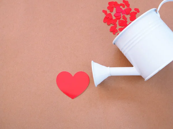 White watering plants and red hearts on brown paper background with copy space. Concept Love and Togetherness.