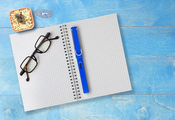 Flat lay blue office wooden desktop with blank notebook and pen with eyeglasses. Top view with space for text. Business and education concept