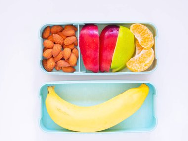 Açık yeşil beslenme çantasındaki taze meyve badem, elma, portakal, muz ve beyaz ahşap arka planda. Yemeği götür. Fotokopi alanı, sağlıklı beslenme kavramları.