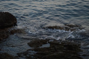 Deniz dalgaları kayalara çarpıyor. Denizde fırtına, karanlık, kasvetli bir fotoğraf. Temiz su, keskin kayalar..