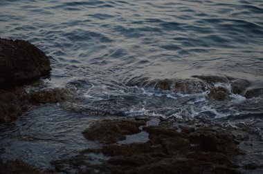 Deniz dalgaları kayalara çarpıyor. Denizde fırtına, karanlık, kasvetli bir fotoğraf. Temiz su, keskin kayalar..