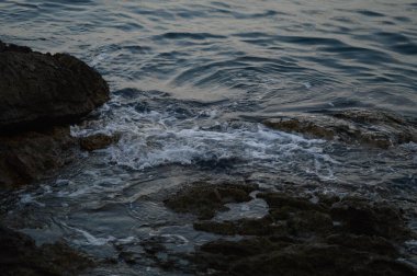 Deniz dalgaları kayalara çarpıyor. Denizde fırtına, karanlık, kasvetli bir fotoğraf. Temiz su, keskin kayalar..