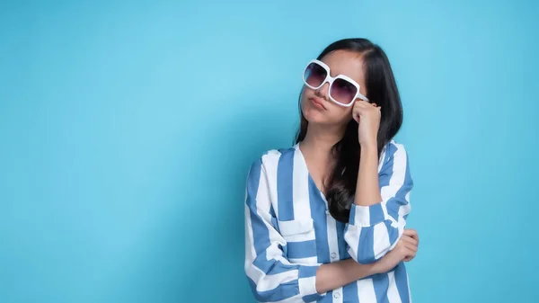 Portrait of young beautiful Asian woman wearing white glasses relax and innocent.cute girl think and consider somethings in studio on blue background.