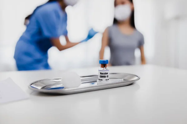 Close up bottle of vaccine on table with woman doctor holding syringe and using cotton before make injection to patient people in medical mask. Covid-19 or coronavirus vaccine