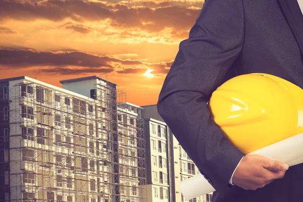 Ingeniero sosteniendo hardhat y plano en la construcción del edificio —  Fotos de Stock