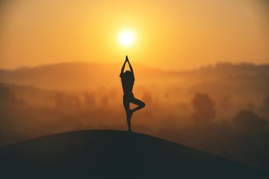 Pratik Yoga muontain üzerinde günbatımında siluet genç kadın