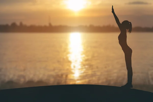 Pratik yoga Nehri üzerinde günbatımında kadın silüeti — Stok fotoğraf