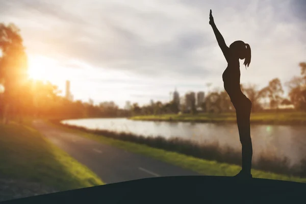 Silueta joven practicando yoga en el parque público al atardecer . — Foto de Stock