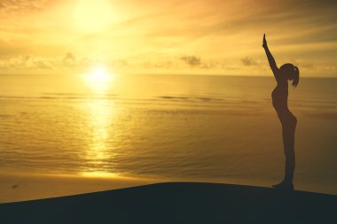 gün batımında sahilde Yoga uygulamak siluet genç kadın.