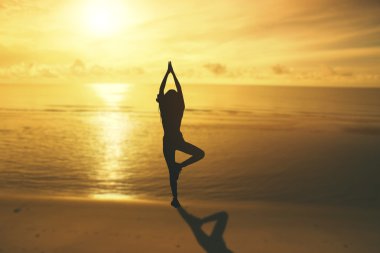 gün batımında sahilde Yoga uygulamak siluet genç kadın.
