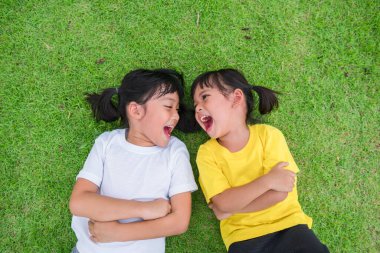 Yeşil çimlerin üzerinde uzanan mutlu Asyalı çocukların yakın çekimi.