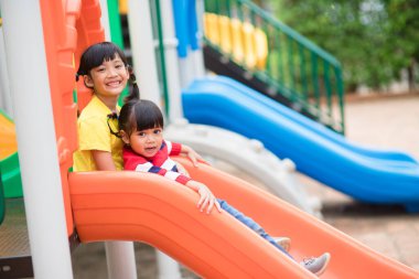 Sevimli küçük kız kardeşler güneşli bir yaz gününde oyun alanında eğleniyorlar. Plastik kaydırak üzerinde çocuklar. Çocuklar için eğlenceli bir aktivite. çocuklar için aktif spor eğlencesi