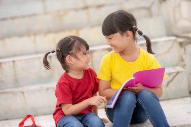 Little Girl and sister reading a book together. Adorable Asian kids enjoying studying outdoors togther. Education, intelligence concept
