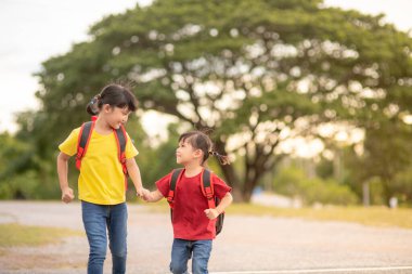 Okula giderken el ele tutuşan şirin Asyalı çocuklar.
