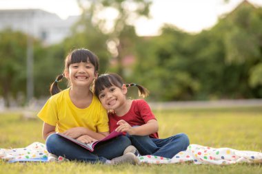 two beautiful little girls reading books in the garden , sitting on grass. The concept of education and friendship.