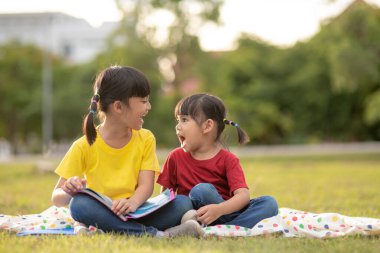 two beautiful little girls reading books in the garden , sitting on grass. The concept of education and friendship.