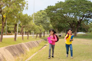 Back to school. Two cute asian child girls with school bag holding book and walk together in the school