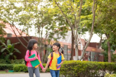 Back to school. Two cute asian child girls with school bag holding book and walk together in the school