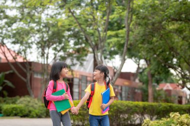 Back to school. Two cute asian child girls with school bag holding book and walk together in the school