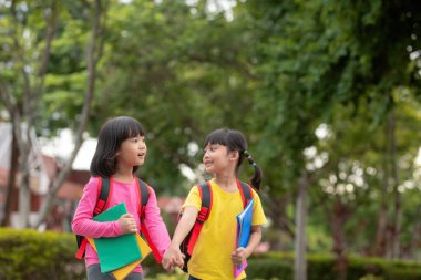 Back to school. Two cute asian child girls with school bag holding book and walk together in the school