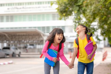 Back to school. Two cute asian child girls with school bag holding book and walk together in the school