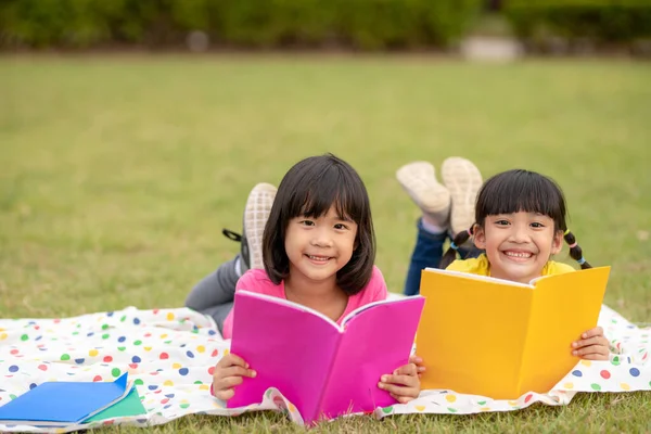 两个漂亮的小女孩坐在草地上 在花园里看书 教育和友谊的概念 — 图库照片