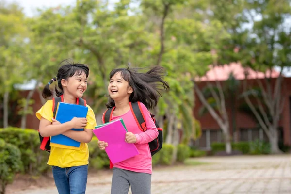 回学校去两个可爱的亚洲女孩拿着书包在学校里一起散步 — 图库照片