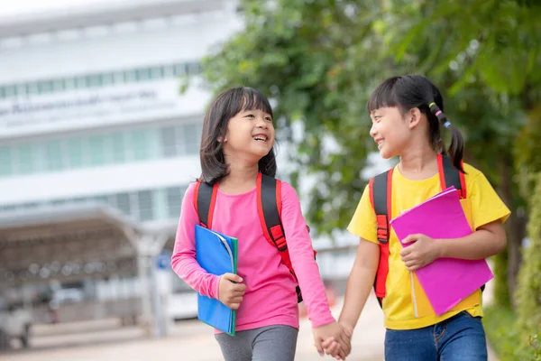 回学校去两个可爱的亚洲女孩拿着书包在学校里一起散步 — 图库照片